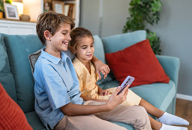 istock Happy children bonding on sofa looking at smartphone 2241403897