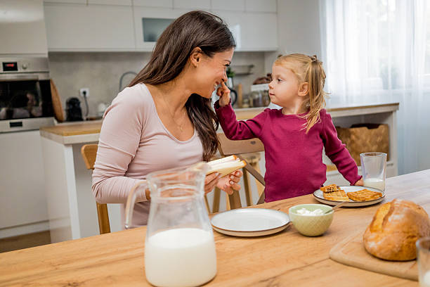 istock Single mother and her little daughter having breakfast together in a bright modern kitchen. Morning sunlight, cozy family atmosphere, and happy moments filled with warmth, care, and love. Concept of positive lifestyle and motherhood 2241404944