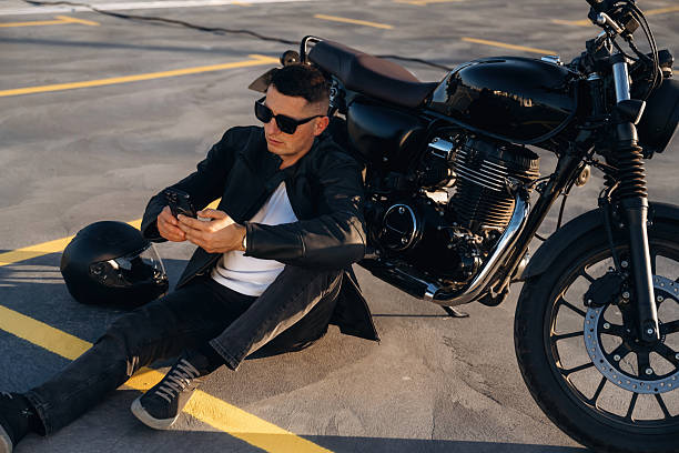 istock Resting, sitting on the ground with smartphone. Man is outdoors with his motorcycle 2241406158