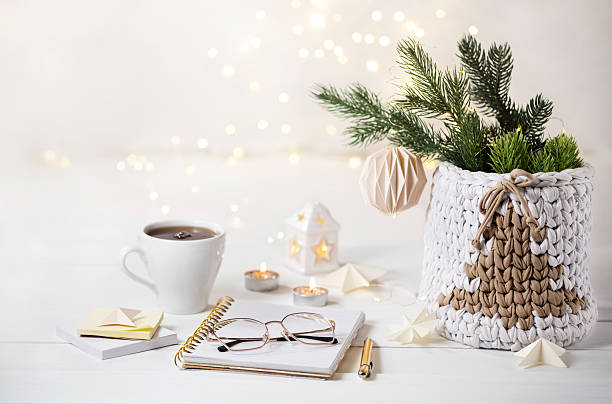 Notepad, pen, glasses, stationery for writing down a plan or a wish list. Cozy Christmas decoration. Knitted basket with Christmas tree on festive lights background
