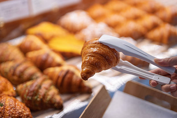 istock Hand picking croissant with tongs in bakery display 2241407992