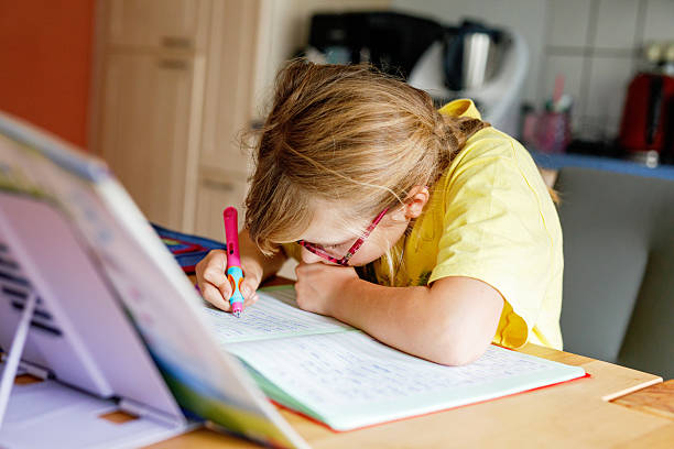 istock Cute elementary school girl writing in her workbook and doing school homework. Focused child learning and studying indoors. Concept of education, childhood, home learning. 2241408130