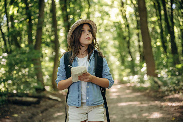 Small notepad is in hands. Young girl hiker is in the forest.