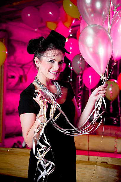 A well dressed beautiful young woman celebrating New Year's Eve. She standing with balloons, looking at camera and smiling.