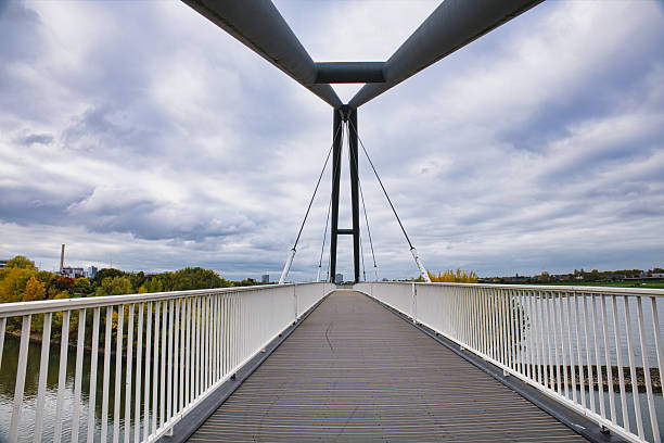 istock Empty Pedestrian Suspension Bridge Over Rhine River with Autumn Trees and Distant Cityscape Under Cloudy Sky in Düsseldorf Germany 2241415501