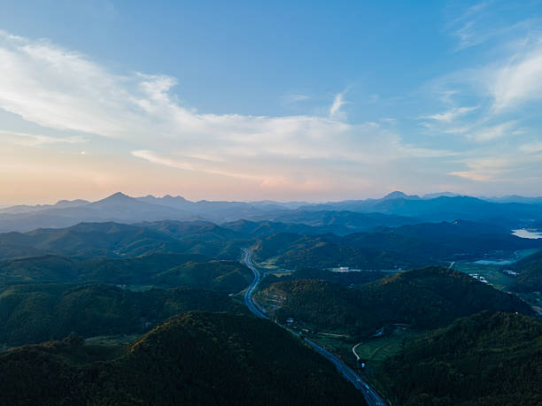 Highway winding through a canyon in the mountains during evening with sunset glow, colorful sky, and serene blue backdrop, aerial view of natural landscape with dramatic mountain scenery and peaceful twilight.