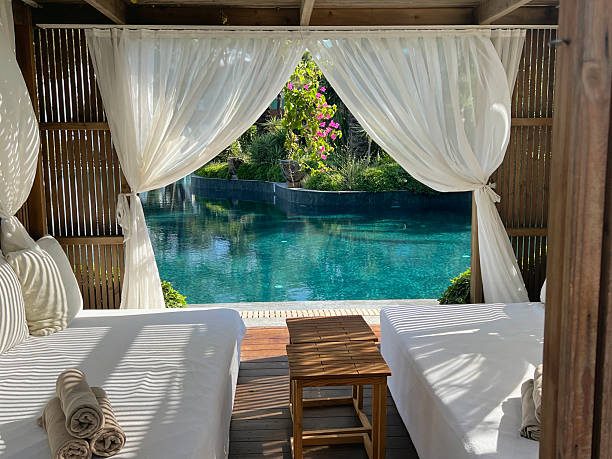 Wooden lounger with white curtains and pool view