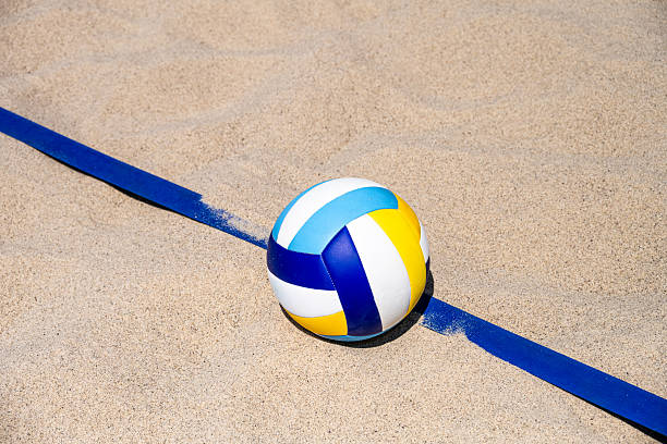 A vibrant beach volleyball ball on sandy terrain with a blue boundary line. Captures the essence of beach volleyball, promoting an active lifestyle and leisure activity. Evokes themes of sports training and healthy living.