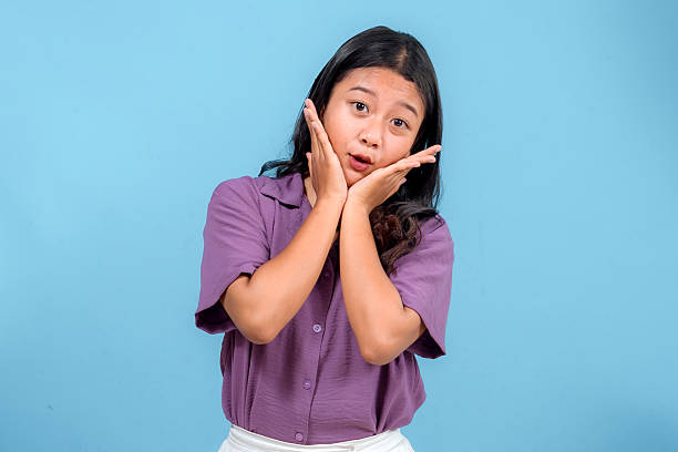 istock Young Asian woman making a surprised and cute facial expression while framing her face with her hands. Ideal for concepts of fun, excitement, creativity, and youthful charm. 2241441762