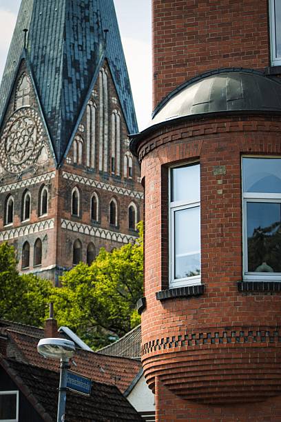 A majestic, brick-built church tower with intricate architectural details stands prominently against a backdrop of lush greenery.