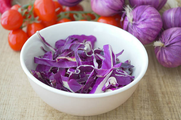 Freshly sliced purple cabbage sits in a bowl beside cherry tomatoes.