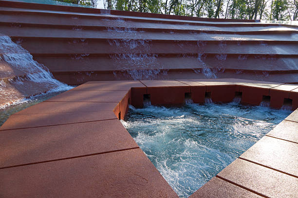 Water cascades down multi-tiered structure, forming abstract, geometric fountain surrounded by transparent glass railing. Amphitheater of water or Canyon in Public city park Krasnodar or Galitsky Park