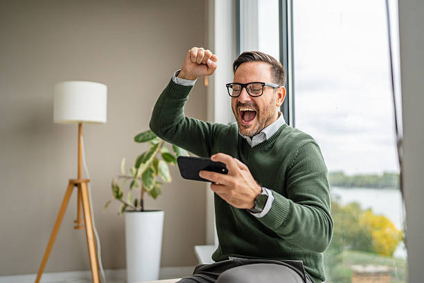 istock Man celebrating online success on smart phone at home 2241457489