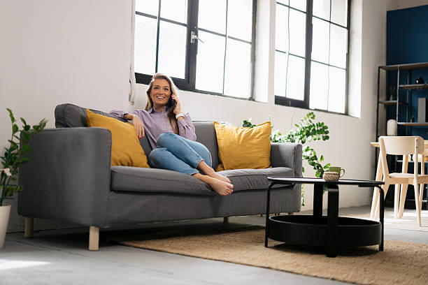 istock Smiling woman sitting on sofa and talking on mobile phone 2241461720
