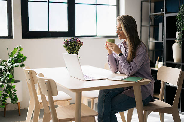 istock Young woman having coffee while working on laptop at home 2241461766