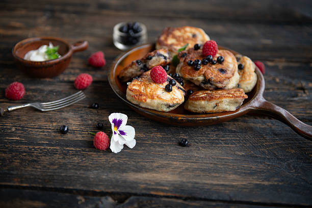 Fresh pancakes decorated with berries and edible flowers on wooden table.