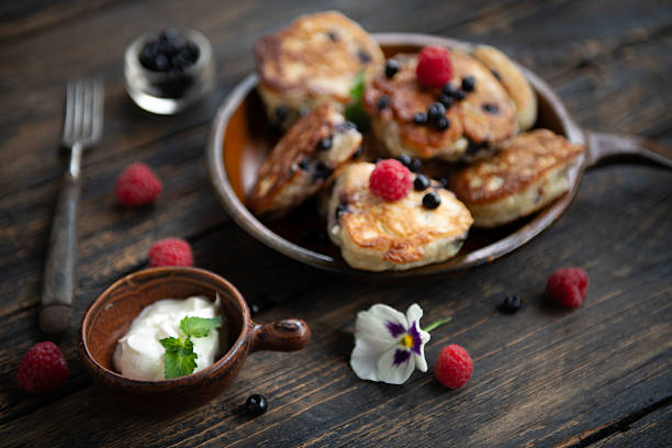 Plate of homemade pancakes topped with raspberries and cream on rustic table.