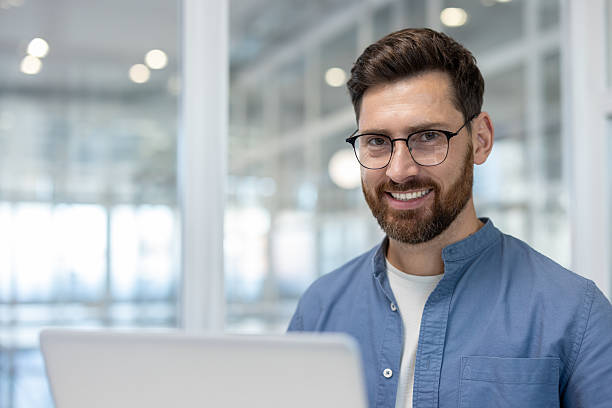 istock Happy man with glasses smiles at the camera in a modern office setting. 2241480617