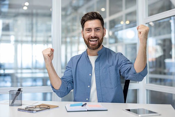 istock Successful man celebrating business victory at office desk 2241481165