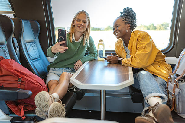 istock Two friends on a train ride sharing a smile, using a phone at a comfy table 2241482120