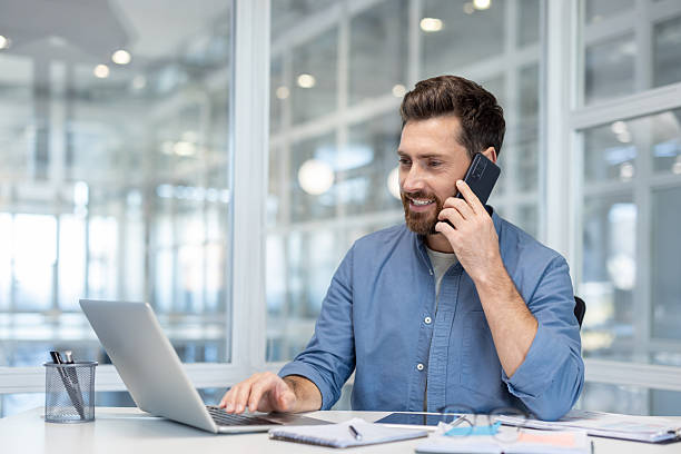 istock Smiling man in office making phone call while working on laptop 2241484871
