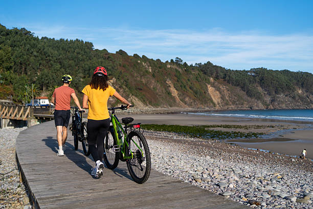 istock Couple walking along coastal boardwalk with e-bikes, enjoying active vacation by beach and ocean cliffs 2241488790