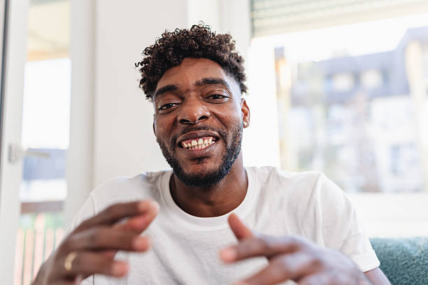 istock Smiling man having a videocall at home, talking and gesturing expressively while wearing a casual white t-shirt. Bright natural light and relaxed atmosphere convey friendliness and confidence 2241489391