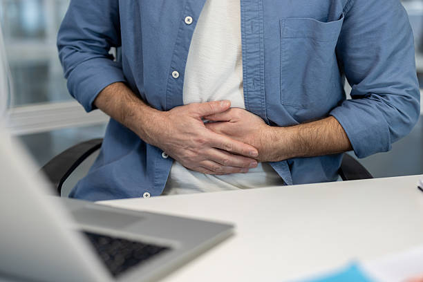 istock A man holds his stomach, likely experiencing abdominal pain while working at his desk. 2241489664