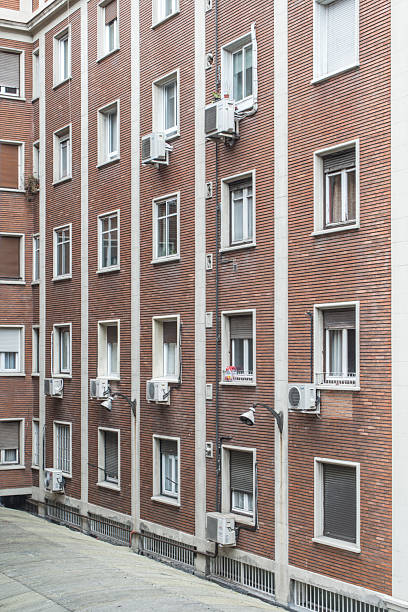 istock Facade of a building with exposed clay-colored brick, windows with air conditioning units and white stone 2241491651