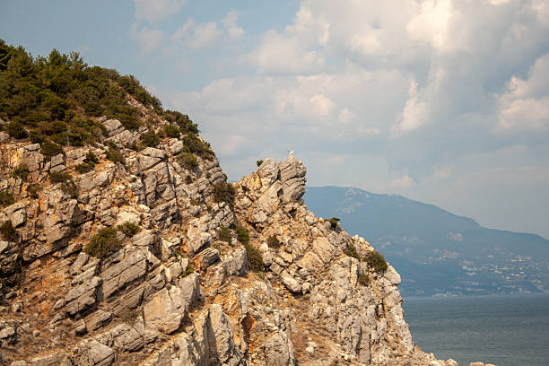 Dramatic landscape scene of rugged shoreline meeting body of water, framed by towering rocky cliffs under bright day