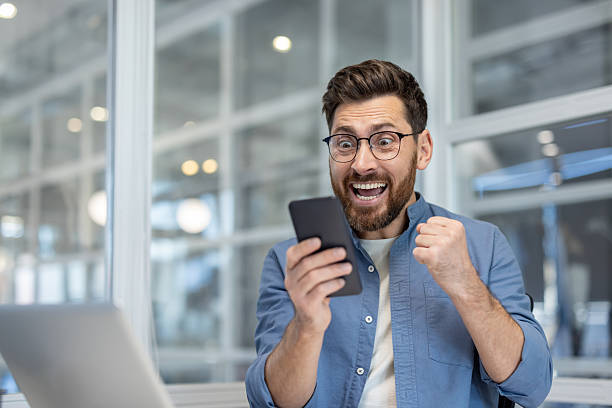 istock Excited business professional celebrates success while checking smartphone in modern office 2241492357