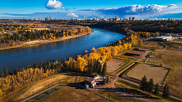 Drone image of a calm river and colorful trees in fall season, captured under dramatic clouds and clear light.