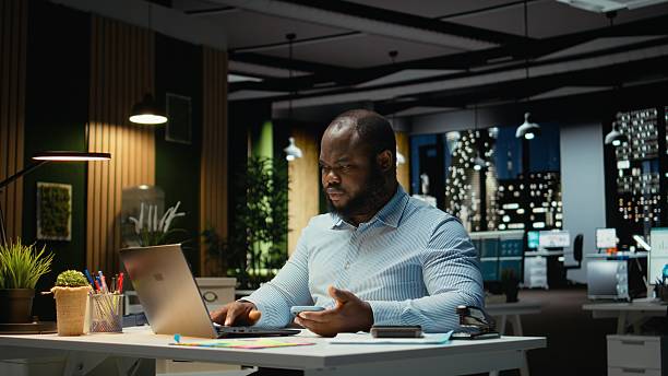 istock Black businessman sighing and checking messages on mobile phone 2241514257