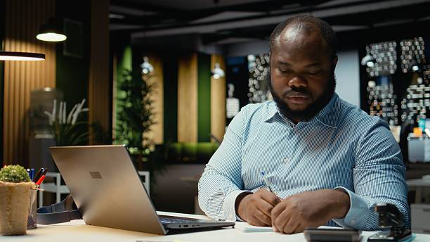 Black guy documenting essential ideas on paper and reading on laptop