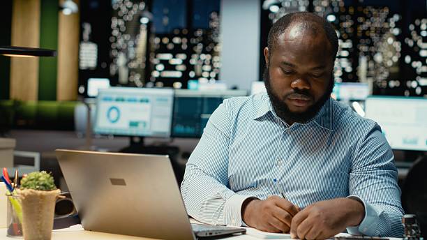 istock Black guy documenting essential ideas on paper and reading on laptop 2241519784
