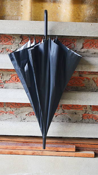 Closed Black Stick Umbrella Against a Rough Concrete and Brick Wall