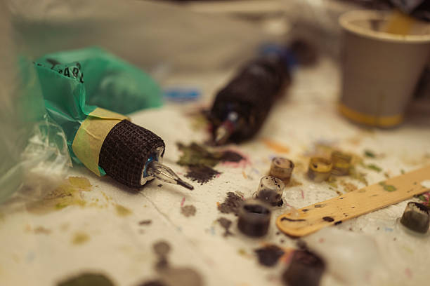 A close-up view of a colorful tattoo machine lying on a workstation surrounded by various tattoo ink caps and tools, showcasing detailed tattoo equipment in a creative workspace environment.