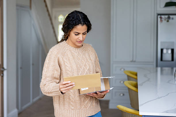 istock Woman at home receiving the mail and reading a letter while holding a package 2241521479