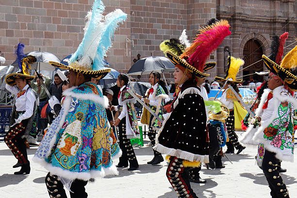 San Juan de los Lagos, Jalisco, Mexico - October 11st, 2025 - Dancers from Tultepec, Mexico State, perform in vibrant, Mariachi-like suits adorned with custom sequin designs and feathered hats. Their capes showcase intricate embroidery, adding flair to their attire, which is complemented by traditional black trousers with sequined patterns. The setting appears to be outdoors, with onlookers under umbrellas. The architectural backdrop features stone walls and arched doorways, typical of Mexican plazas, enhancing the cultural ambiance. The dancers energetic posture highlights the dynamic nature of the folkloric dance.