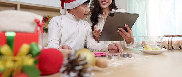 istock Digital Baking Guide. A mother and son exploring Christmas cookie recipes on a tablet in a festive kitchen. 2241543778
