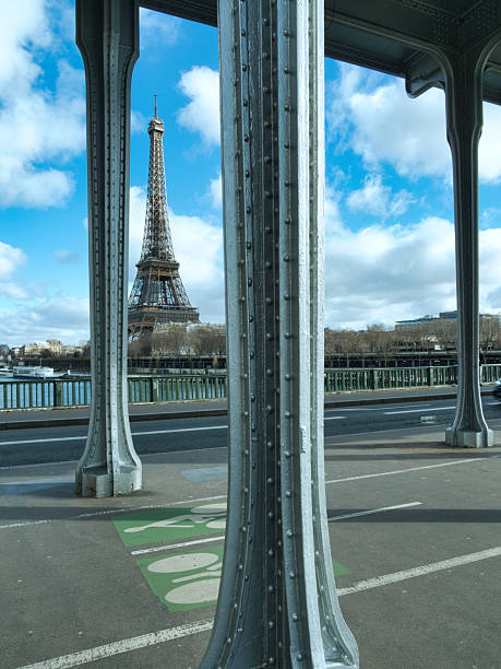 istock Eiffel Tower View from Bir-Hakeim Bridge - The Eiffel Tower prominently featured against a bright blue sky with white clouds, framed by the grey metal structure and lampposts of the Pont de Bir-Hakeim in Paris. 2241547665