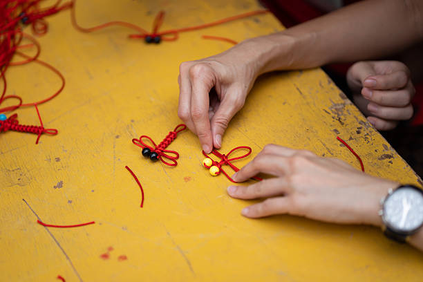 istock Hands crafting a traditional Chinese knot with red string to make a dragonfly on a yellow table. 2241549781