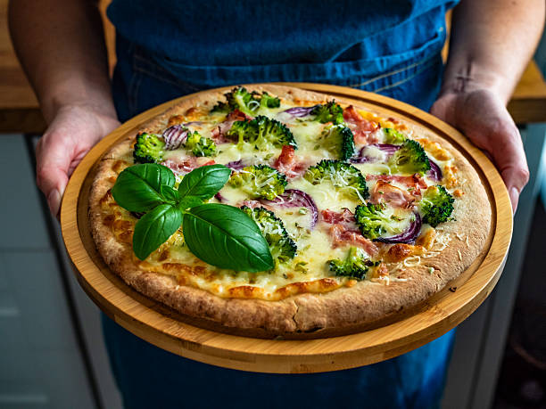 istock Woman holding circle pizza broccoli with bacon and mozzarella cheese on cutting board 2241550632
