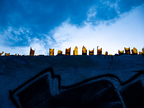 Broken Glass Bottles Embedded in Concrete Wall Against Blue Sky - Security Barrier and Urban Defense System
