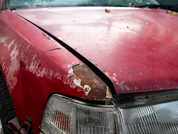 Severe rust corrosion and peeling paint damage on red car hood edge above headlight showing metal deterioration