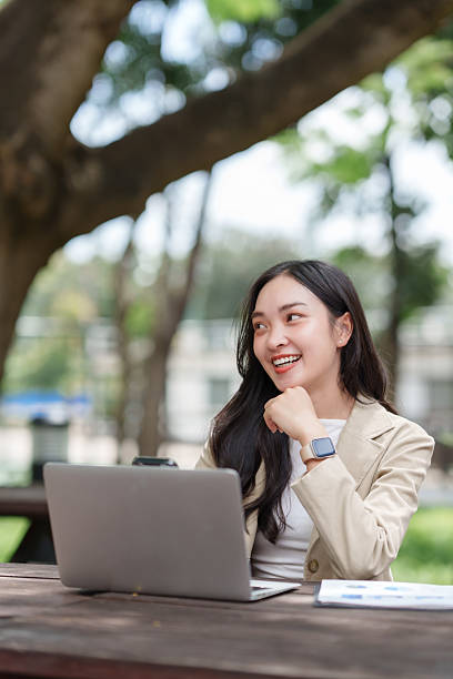 istock Woman working remotely on laptop outdoors, smiling and thinking 2241557534
