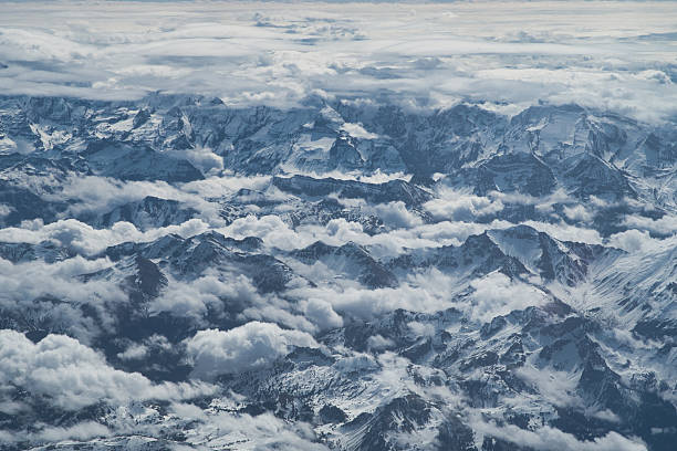 istock Dramatic Snow-Covered Alps and Clouds - Stunning aerial view capturing the rugged, snow-covered mountain peaks of the Alps, emerging from a thick layer of swirling white clouds. 2241558298