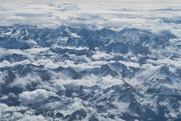 istock Dramatic Snow-Covered Alps and Clouds - Stunning aerial view capturing the rugged, snow-covered mountain peaks of the Alps, emerging from a thick layer of swirling white clouds. 2241558309