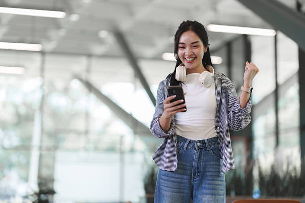 istock Young asian woman celebrating success using smartphone 2241560573