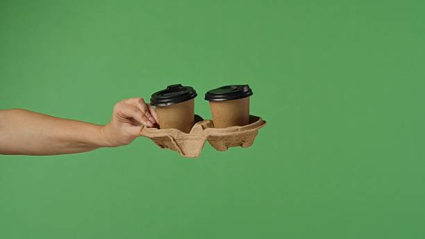 istock Woman Hand Holding Two Coffee Cups with Green Background 2241562844
